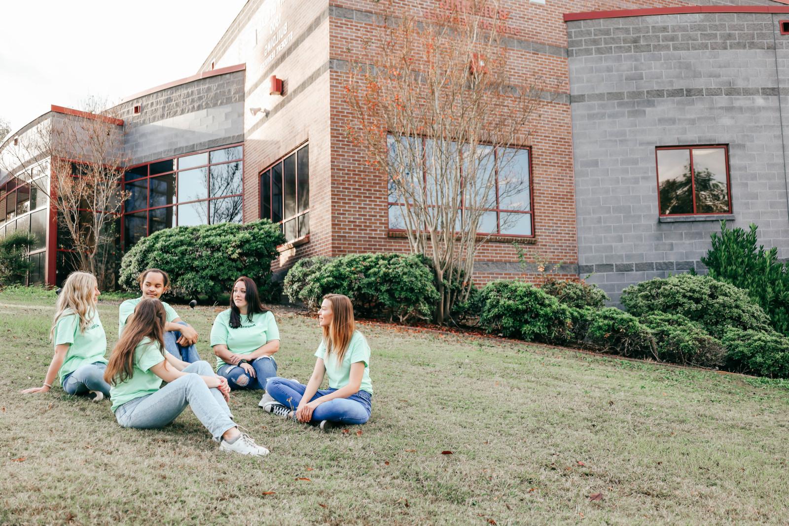 A group of students all wearing mint green 买世界杯app推荐 shirts sit on the lawn to the left of the 1300 bldg chatting.